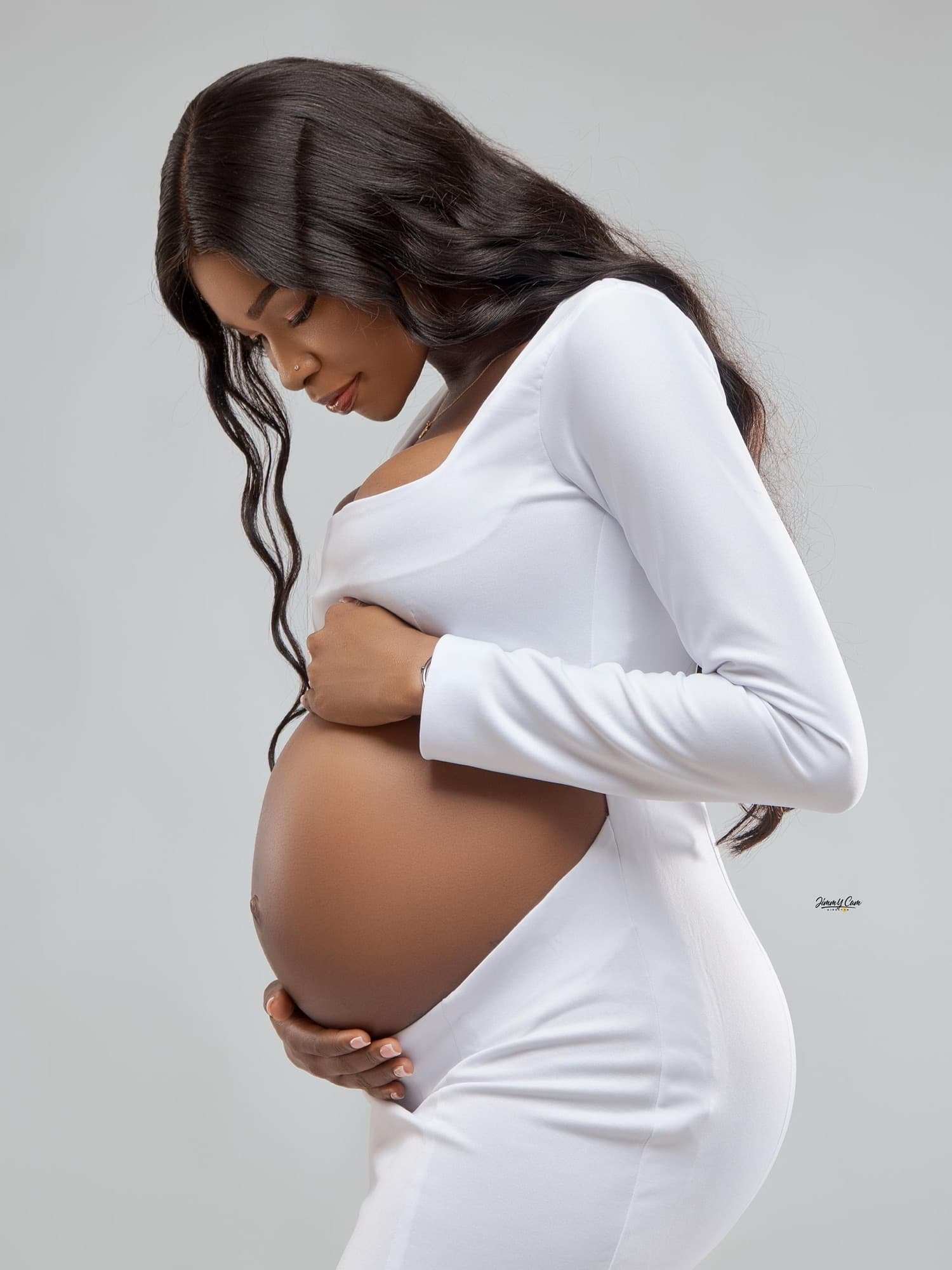 Future maman en robe blanche, de profil, les mains sur le ventre